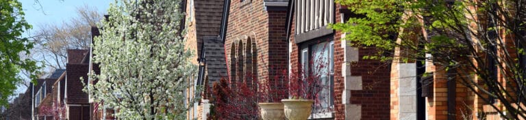 Row of brick townhouses with blooming trees, arched windows, and springtime greenery.