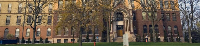 Historic brick building with arched entrance, trees, and a statue on the front lawn.