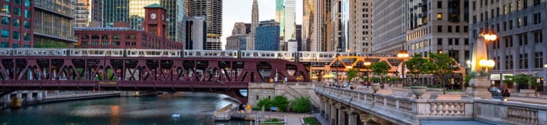 Cityscape with river, bridge, elevated train, and tall buildings during daylight.