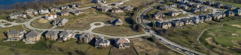 Aerial view of a suburban neighborhood with houses, circular road, golf course, and surrounding greenery.