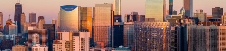 Cityscape with high-rise buildings bathed in golden light at sunrise or sunset.