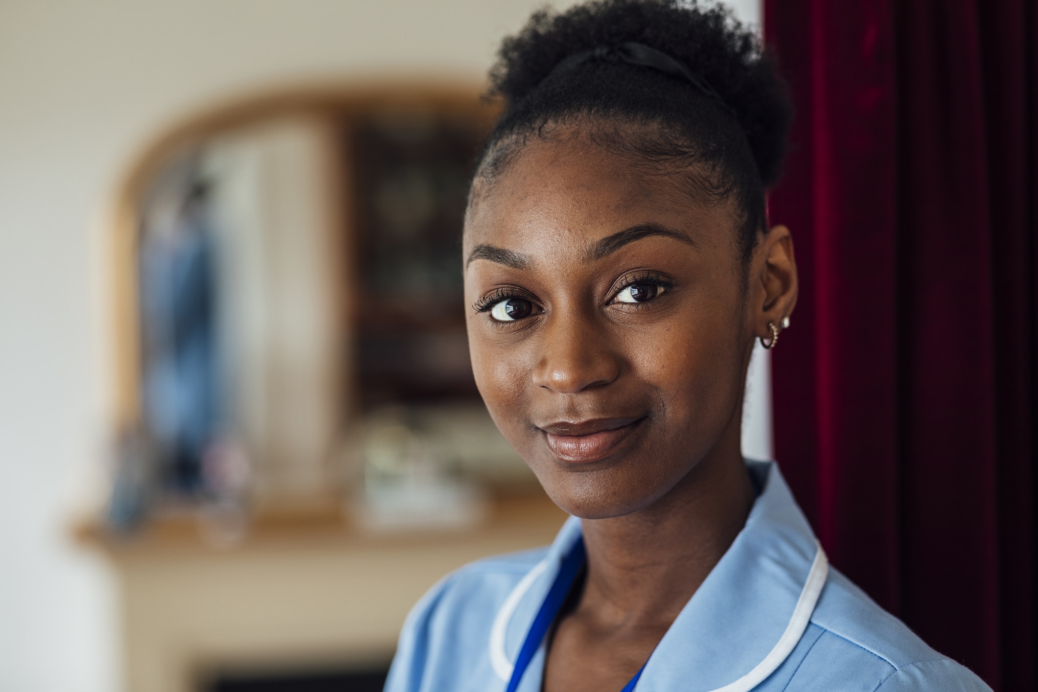 Headshot of a nurse at a patient's home doing a house call in the North East of England. She dressed in her uniform, looking at the camera while smiling.