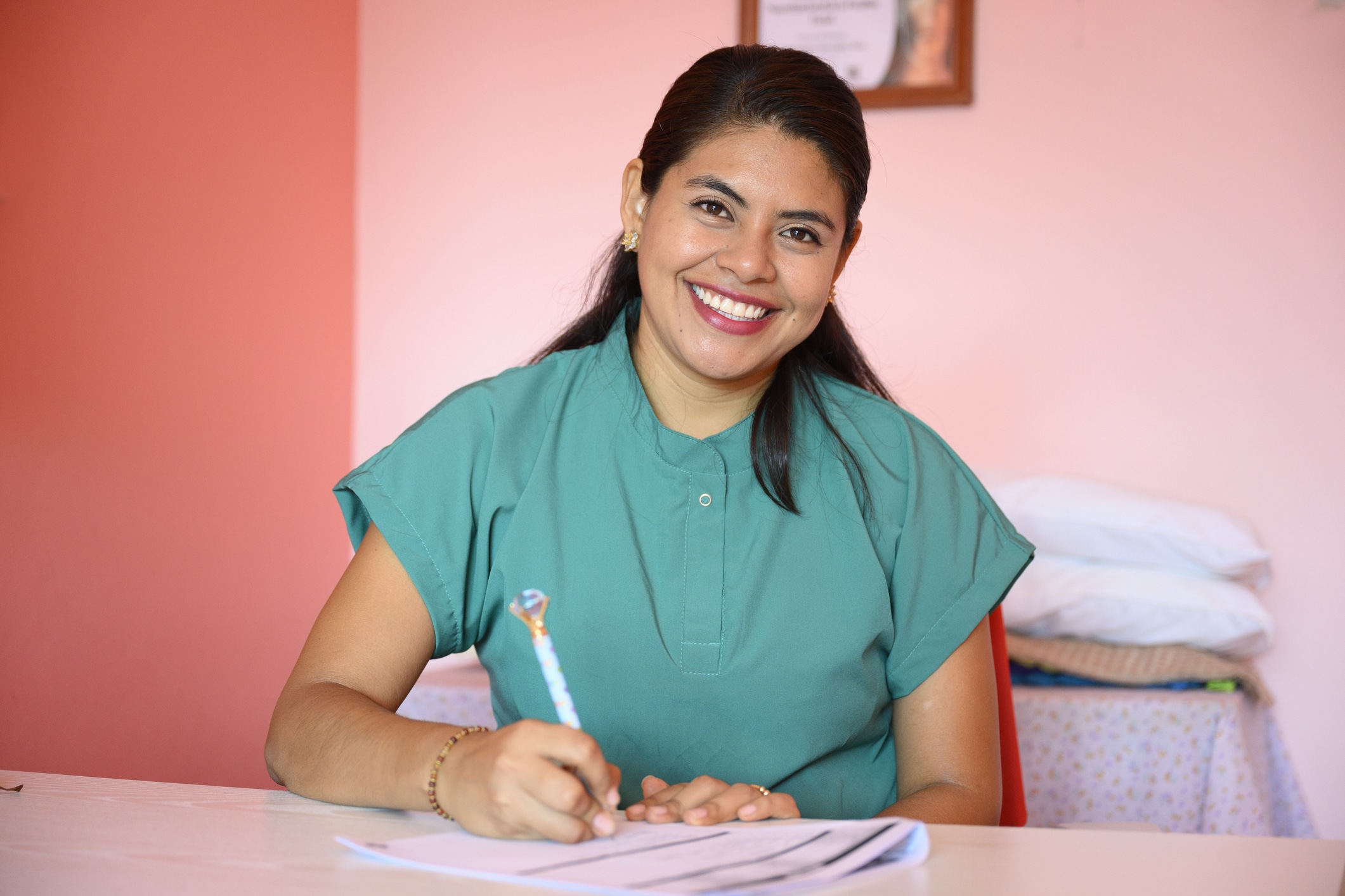 Happy latin female doctor smiling while writing medical notes at her office desk, showcasing professionalism and expertise in healthcare. Concentrated and optimistic, she engages with her work