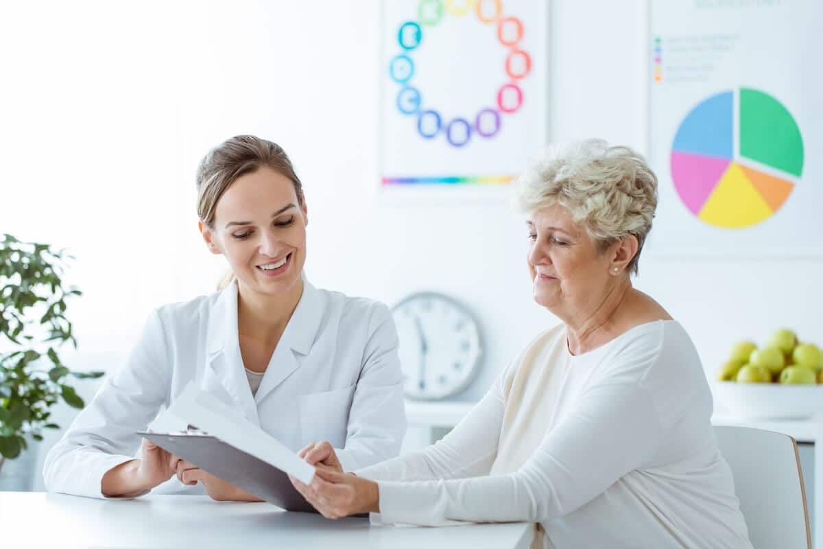 A woman and a doctor sit at a table, discussing a folder filled with medical documents.